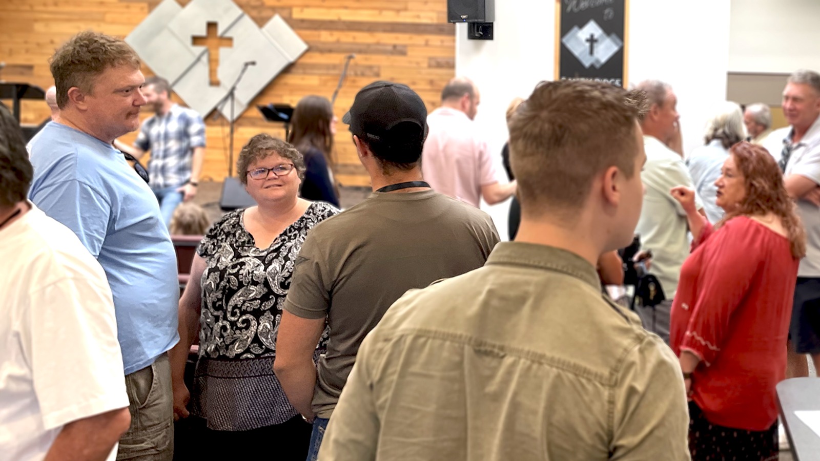 The congregation of Sandy Ridge Church talking together in the sanctuary beneath the wooden cross after a Sunday service